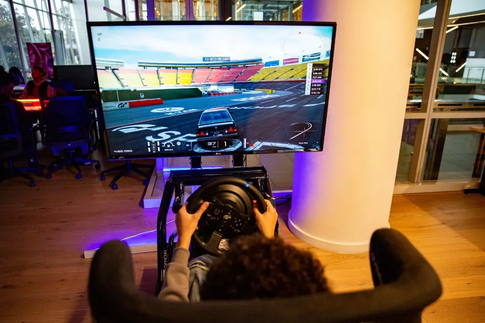 Learner playing a racing video game on a large screen using a steering wheel controller