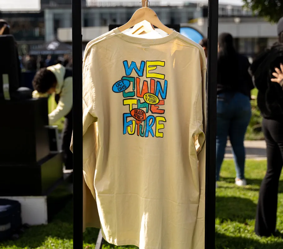 Cream long-sleeve tee on a hanger with a colourful “We own the future” print from the UCT OHS x Grade Africa collection