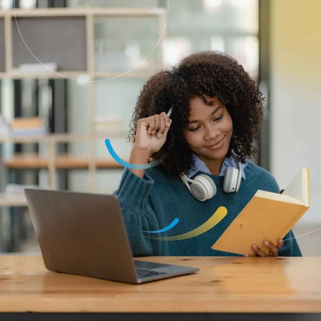 A learner reading a notebook at a desk beside her laptop